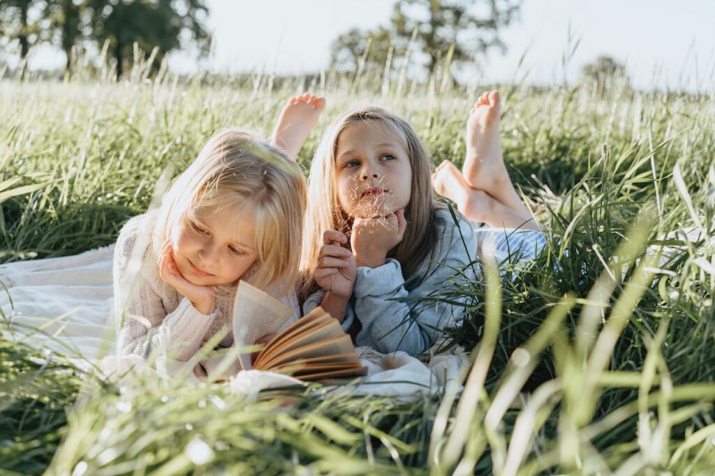 Little girls lying on green grass field on a summer morning.